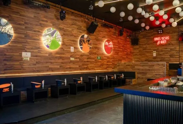 Antro Santa Fe 1 — área de mesas junto a muro de madera con ventanas circulares iluminadas