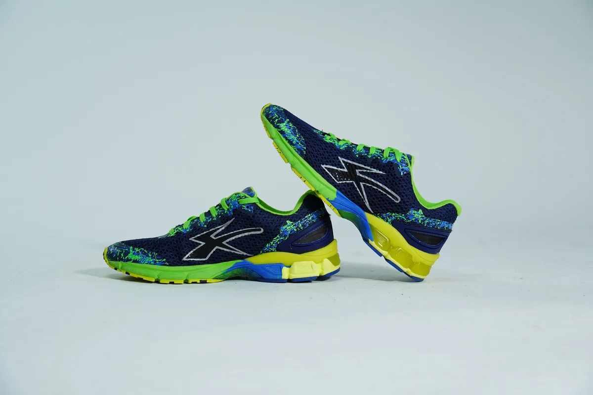 Foto de producto para e-commerce: tenis para correr verde con azul en estudio, toma 110