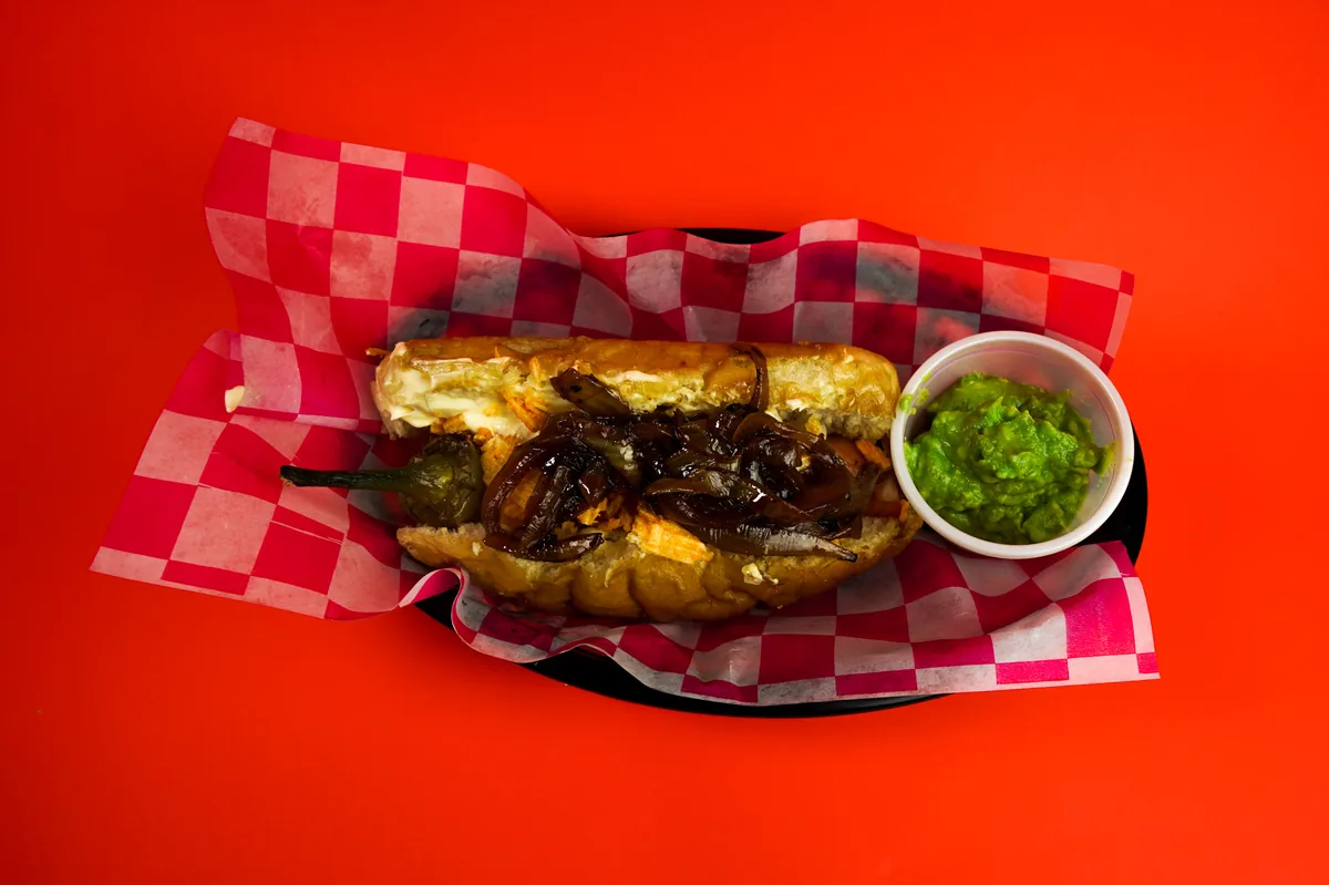 Fotografía de alimentos en estudio: hot dog con guacamole sobre fondo rojo, toma 47