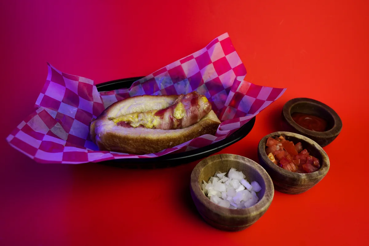 Fotografía de alimentos en estudio: hot dog con salsas sobre fondo rojo, toma 27