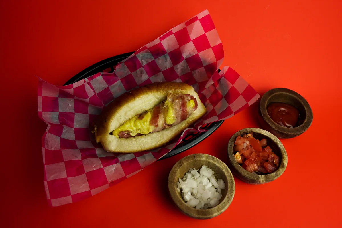 Fotografía de alimentos en estudio: hot dog con salsas sobre fondo rojo, toma 28