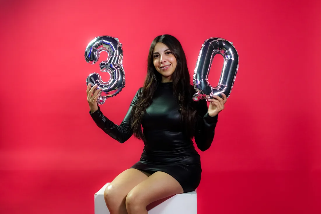 Sesión de fotos de cumpleaños en estudio con vestido negro y números plateados sobre fondo rojo, toma 1