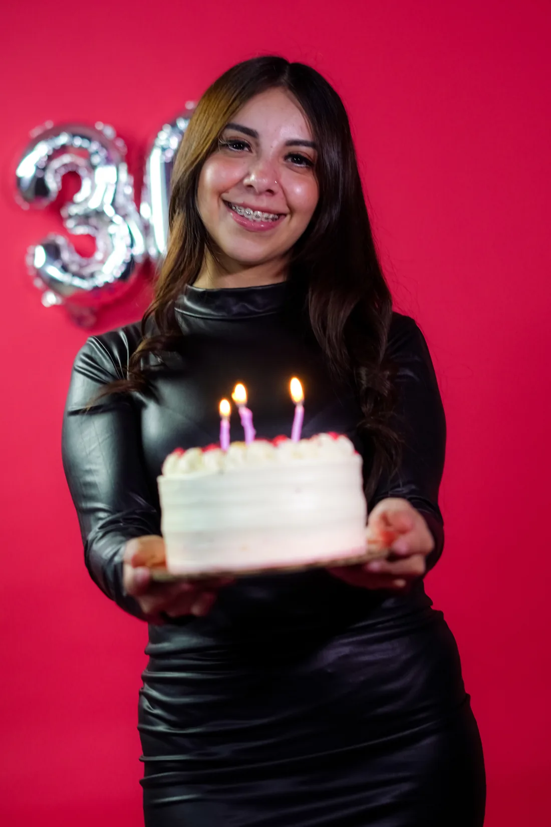 Sesión de fotos de cumpleaños en estudio con vestido negro y números plateados sobre fondo rojo, toma 7