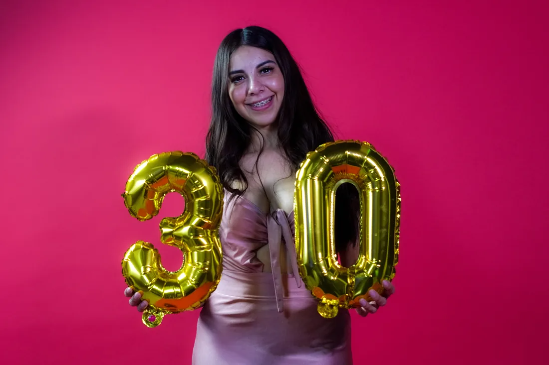 Sesión de fotos de cumpleaños en estudio con vestido rosa y números dorados sobre fondo rosa, toma 12