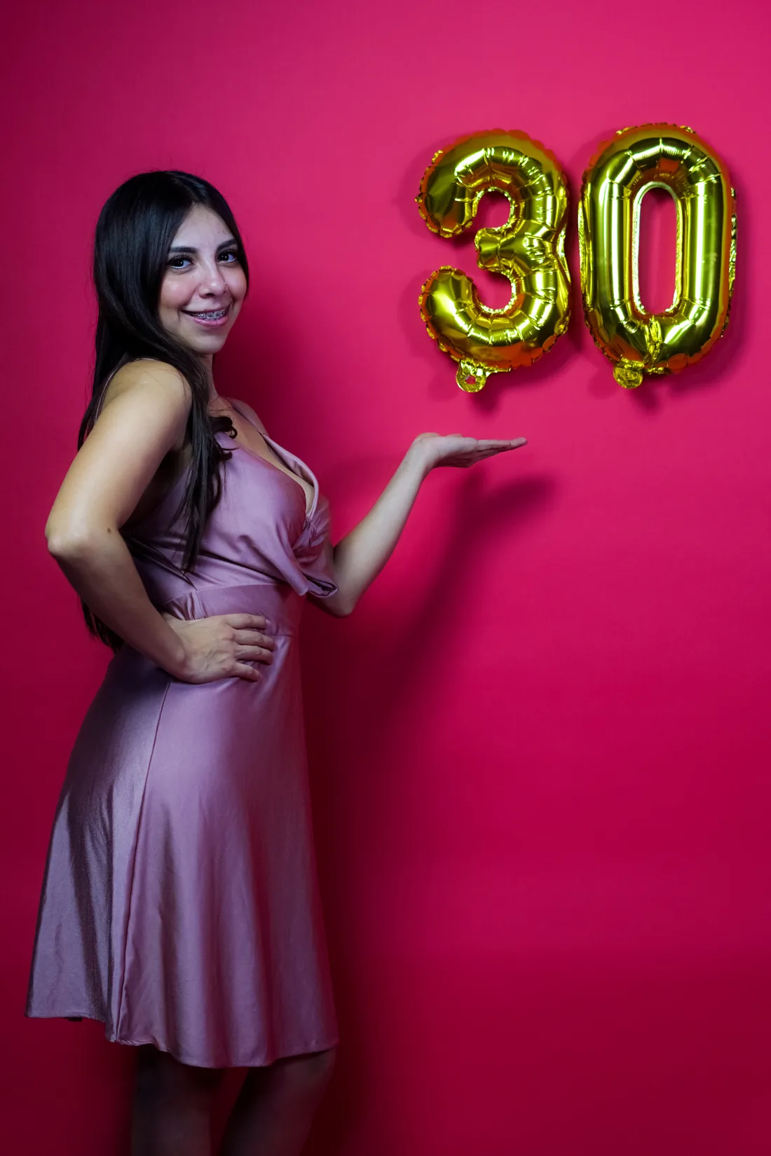 Sesión de fotos de cumpleaños en estudio con vestido rosa y números dorados sobre fondo rosa, toma 13