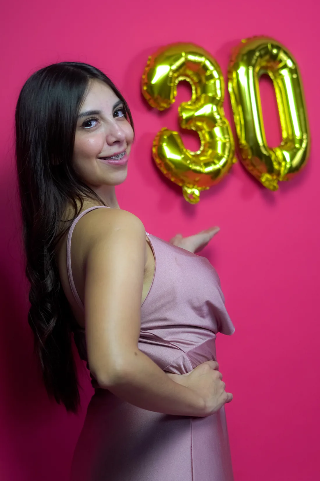 Sesión de fotos de cumpleaños en estudio con vestido rosa y números dorados sobre fondo rosa, toma 17