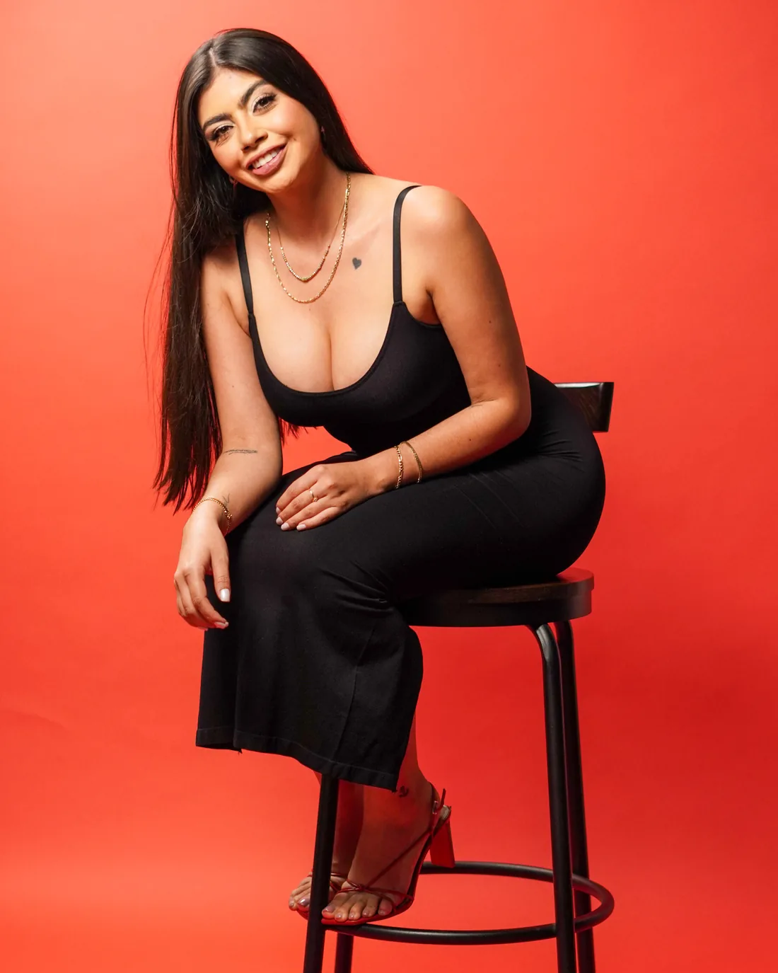Sesión de fotos en estudio con top negro en banco alto sobre fondo rojo