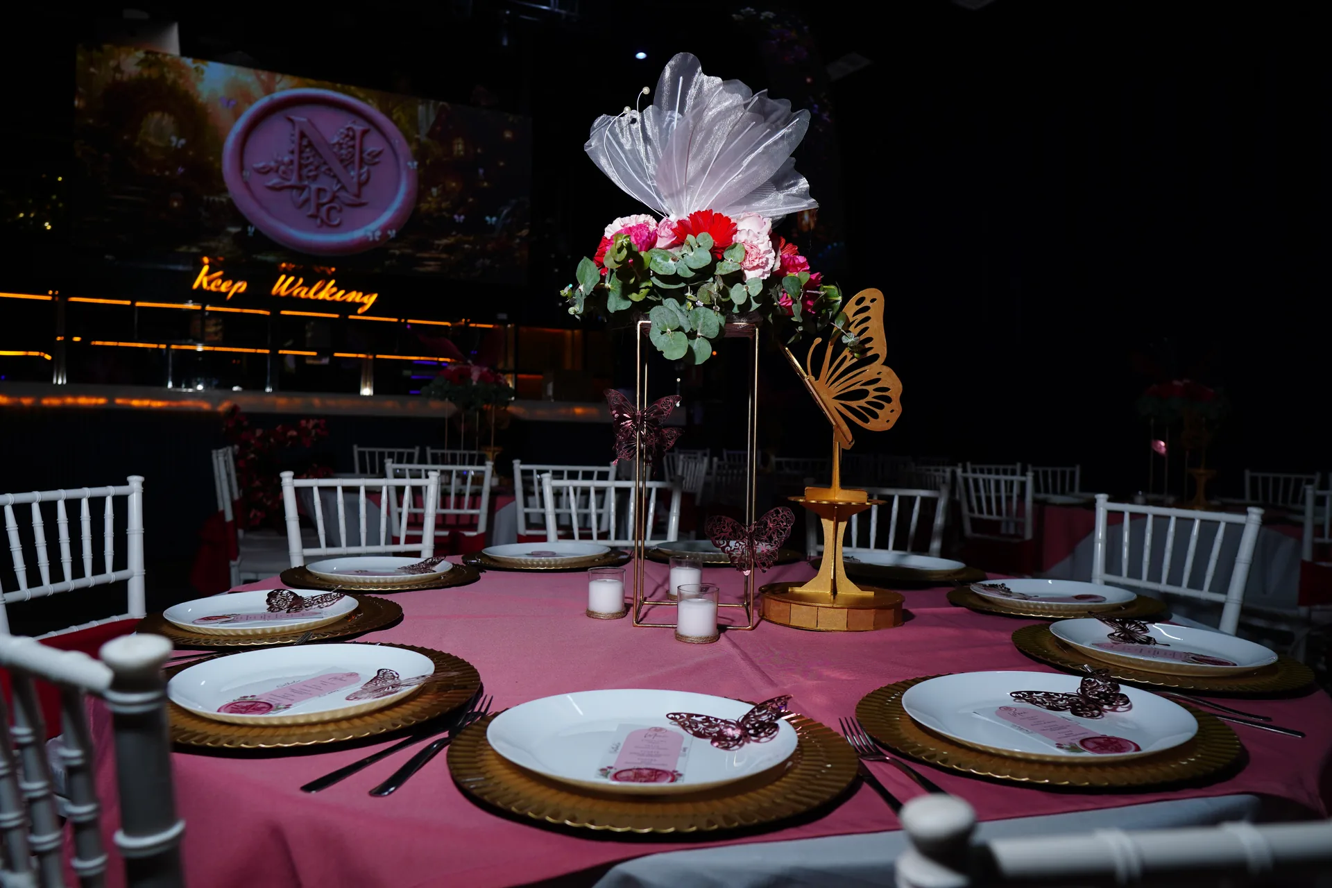 Mesa de XV años vestida con mantel rosa, platos dorados y centro de mesa alto