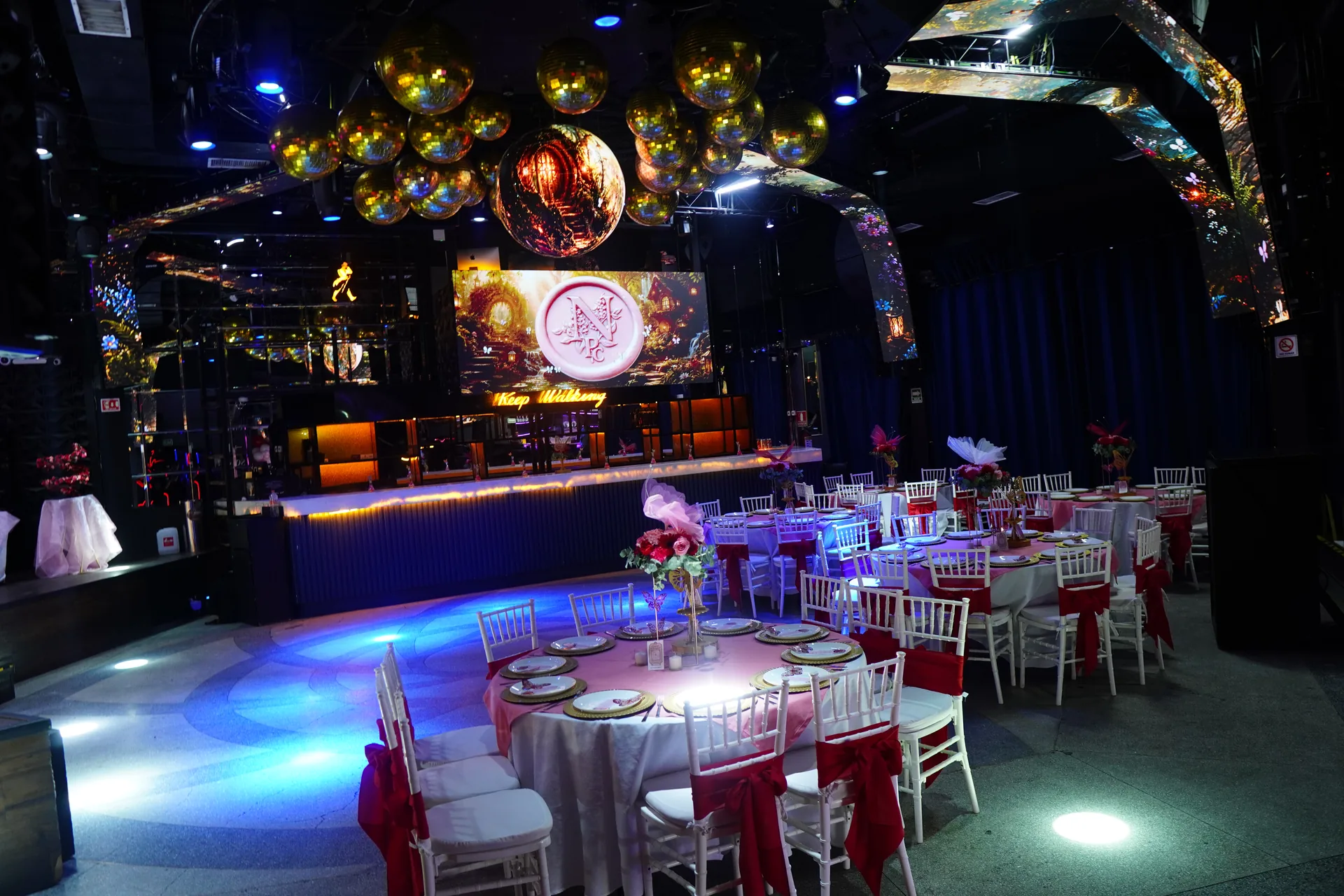 Salón de XV años con globos metálicos dorados, pantallas y mesas montadas